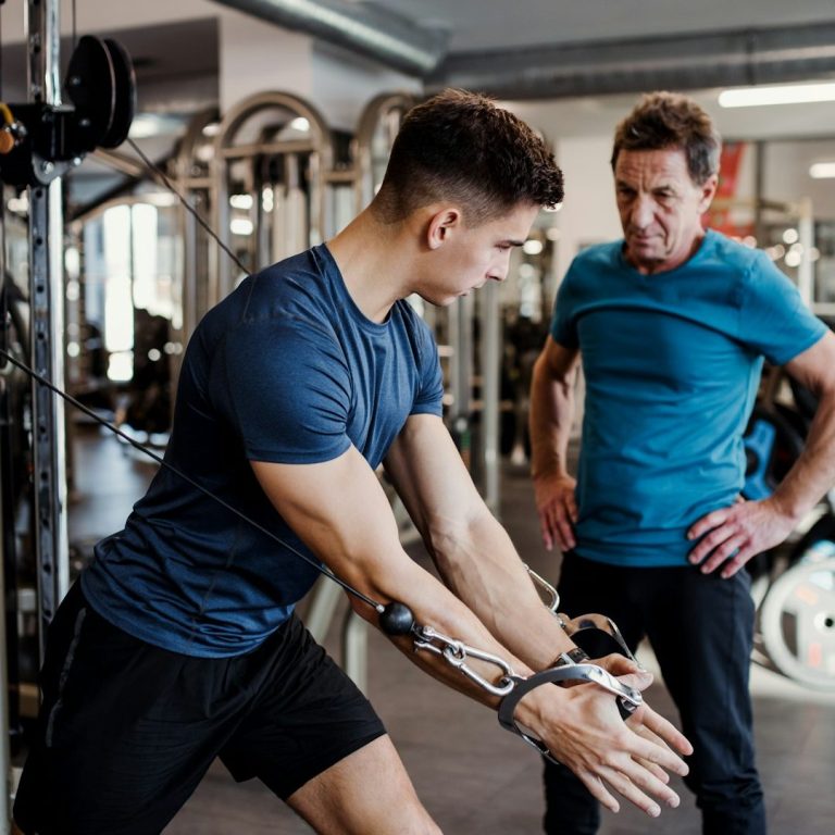 Junger Mann trainiert im Fitnessstudio mit Anleitung eines Trainers.