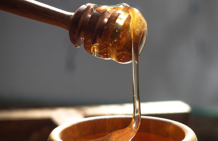 Honig tropft von einem Holzlöffel in eine Schale.