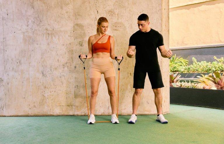 Frau trainiert mit Widerstandsband, unterstützt von einem Trainer in Sportkleidung.